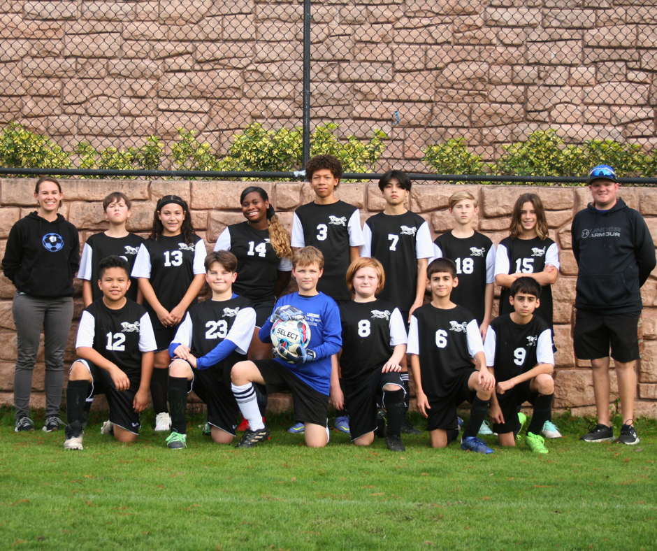 a team picture of the coed private middle school soccer team at Lakeside Christian School pose in their black home game jerseys while standing on a green soccer field with their two Christian coaches